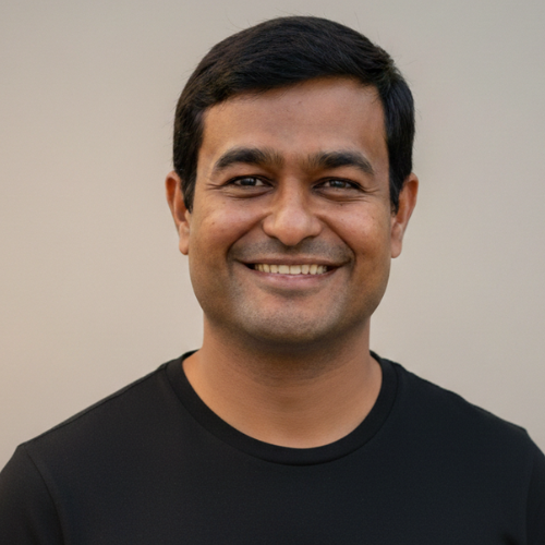 Smiling headshot of a person with short dark hair wearing a plain black crewneck shirt, centered against a soft beige-to-gray gradient background.